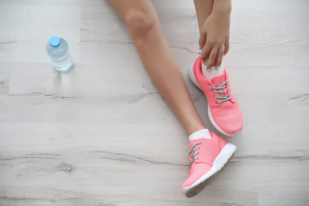 Person preparing to stretch in pink athletic shoes, with a water bottle nearby, emphasizing the importance of daily stretching for winter wellness and injury prevention.