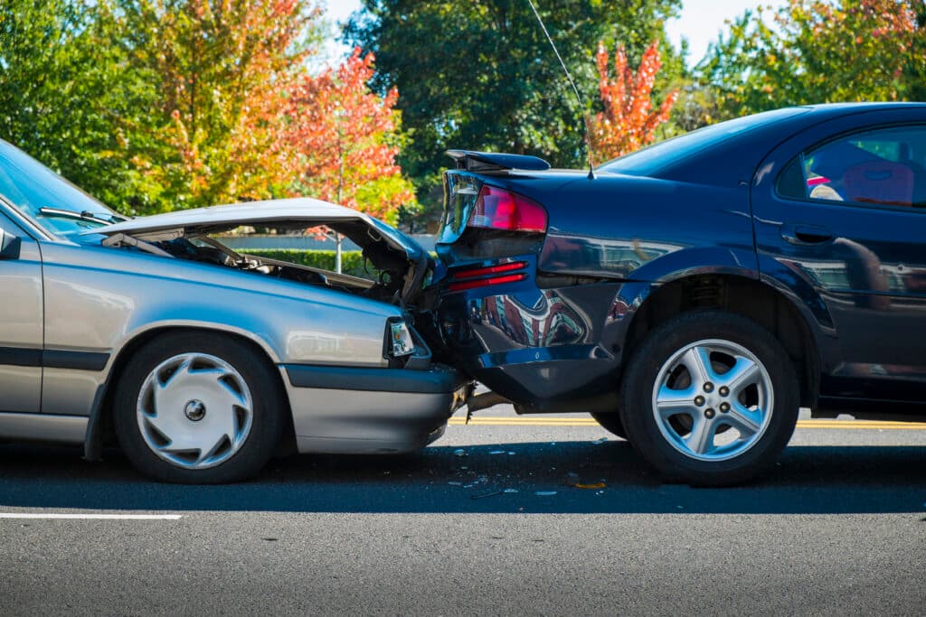 Car accident scene showing a silver vehicle with a raised hood and a black vehicle with rear damage, emphasizing the impact of auto collisions and the need for chiropractic care for injury recovery.