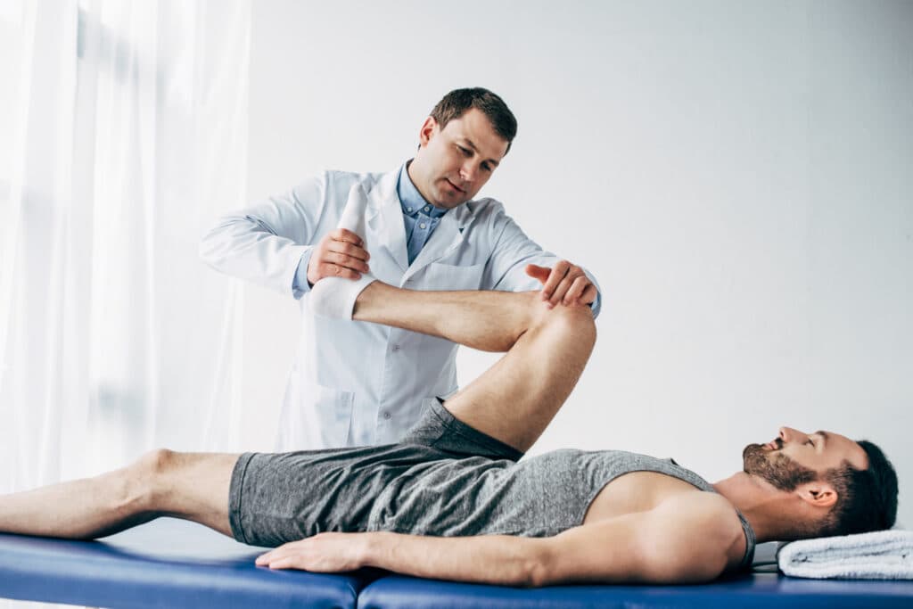 Chiropractor performing stretching technique on a male patient to enhance flexibility and joint mobility in a clinical setting.