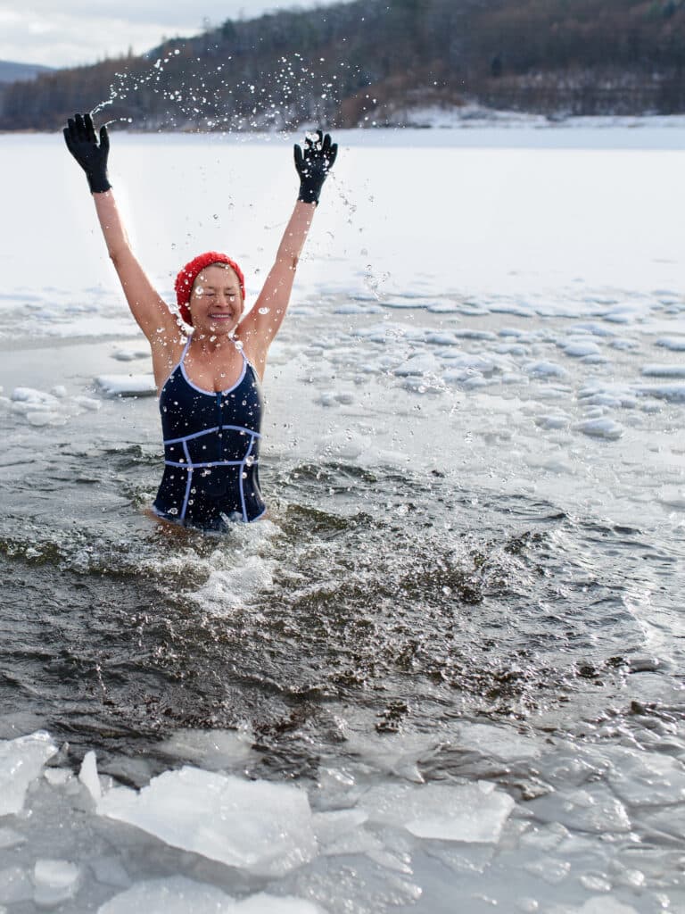 Person in a swimsuit and red hat joyfully splashing in icy water, demonstrating the invigorating experience of ice baths for therapeutic benefits.