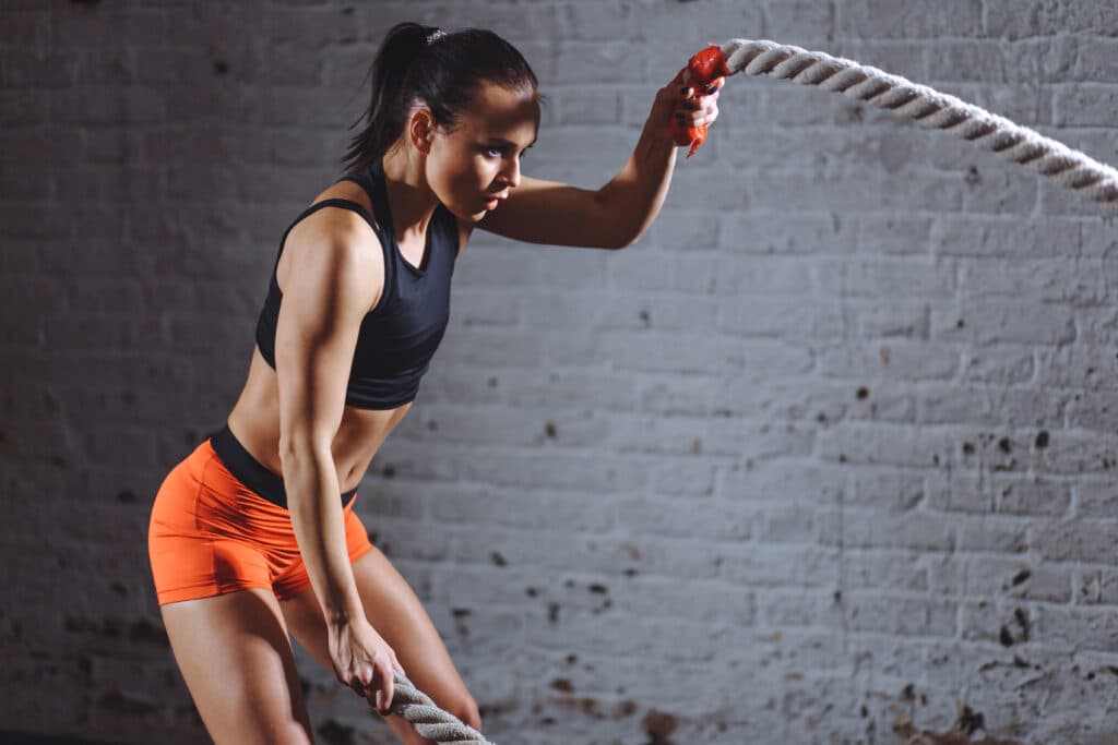 Athlete performing battle rope exercises in a gym, showcasing strength training and fitness recovery benefits related to ice baths.