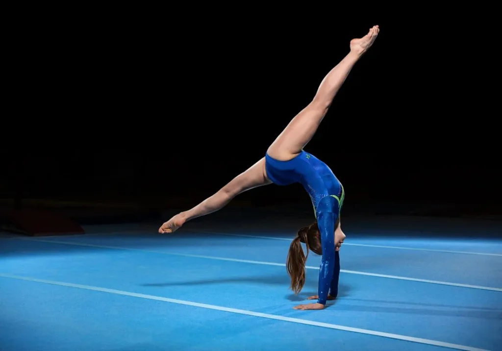 Gymnast performing a handstand on blue mat, showcasing strength and flexibility, relevant to chiropractic care for injury prevention and performance enhancement in gymnastics.